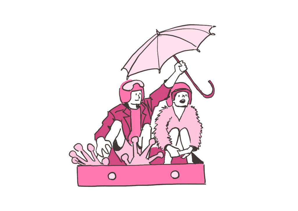 Zwei Leute sitzen in einem Koffer. Beide Leute tragen einen Helm. Eine Person hat Froschfüße. Diese Person hält einen Regenschirm über beide.