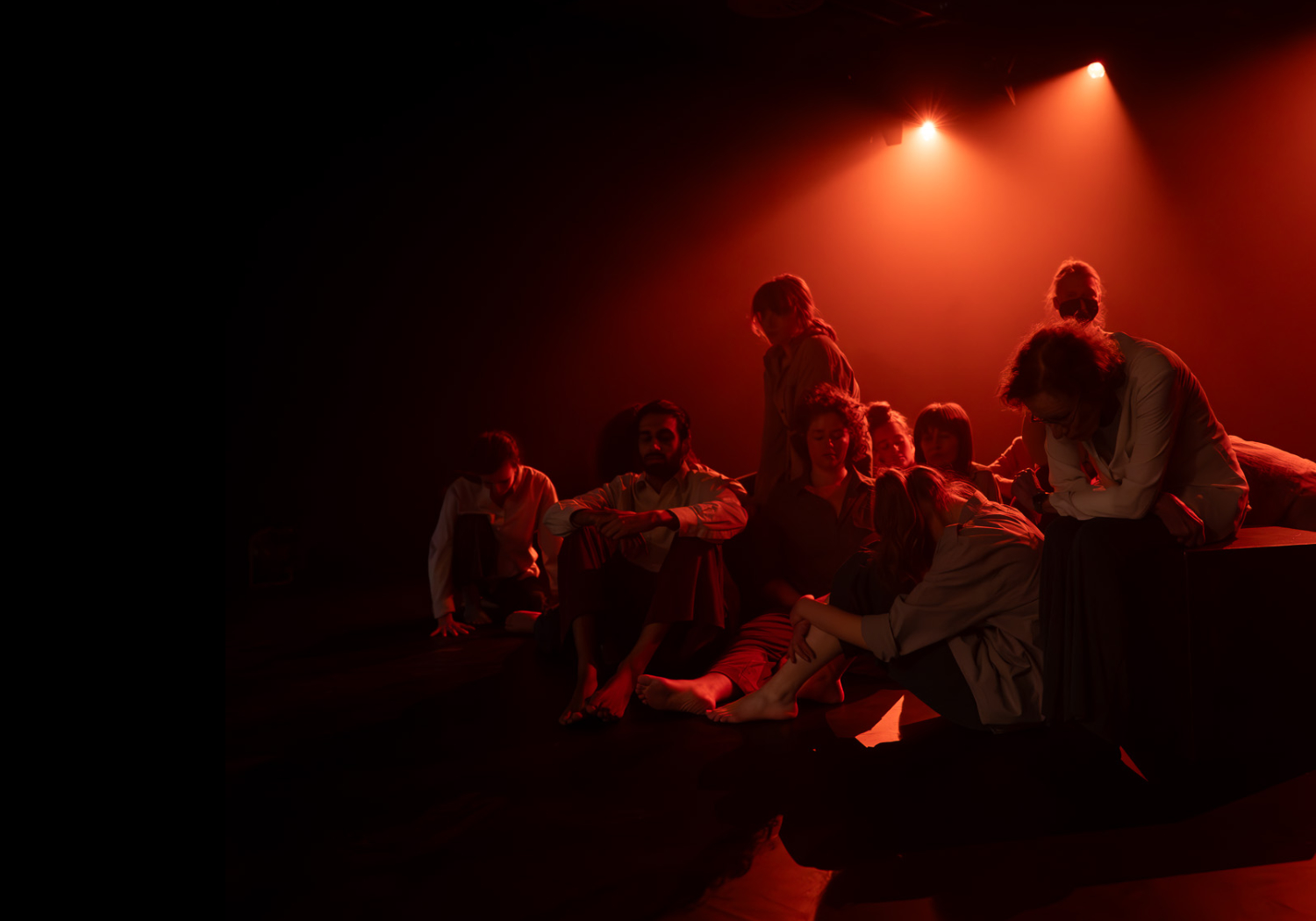 Eine Gruppe junger Menschen, die auf einer Bühne sitzen. Die Bühne ist in rotes Licht getaucht.